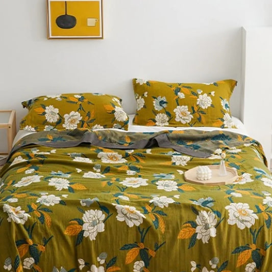 Olive green throw blanket with hand-drawn ivory, gold, and indigo floral details, styled on neutral bedding