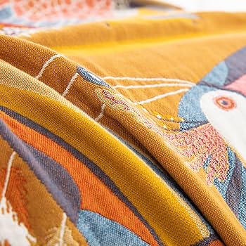 Sol Tropicana bed throw on linen bed with natural sunlight, featuring toucan motifs and citrus hue