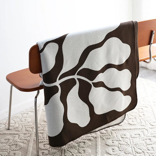 jacquard-knit throw is crafted in a soft acrylic weave, featuring a bold abstract pattern in rich brown and muted stone.