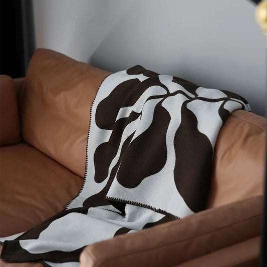 jacquard-knit throw is crafted in a soft acrylic weave, featuring a bold abstract pattern in rich brown and muted stone